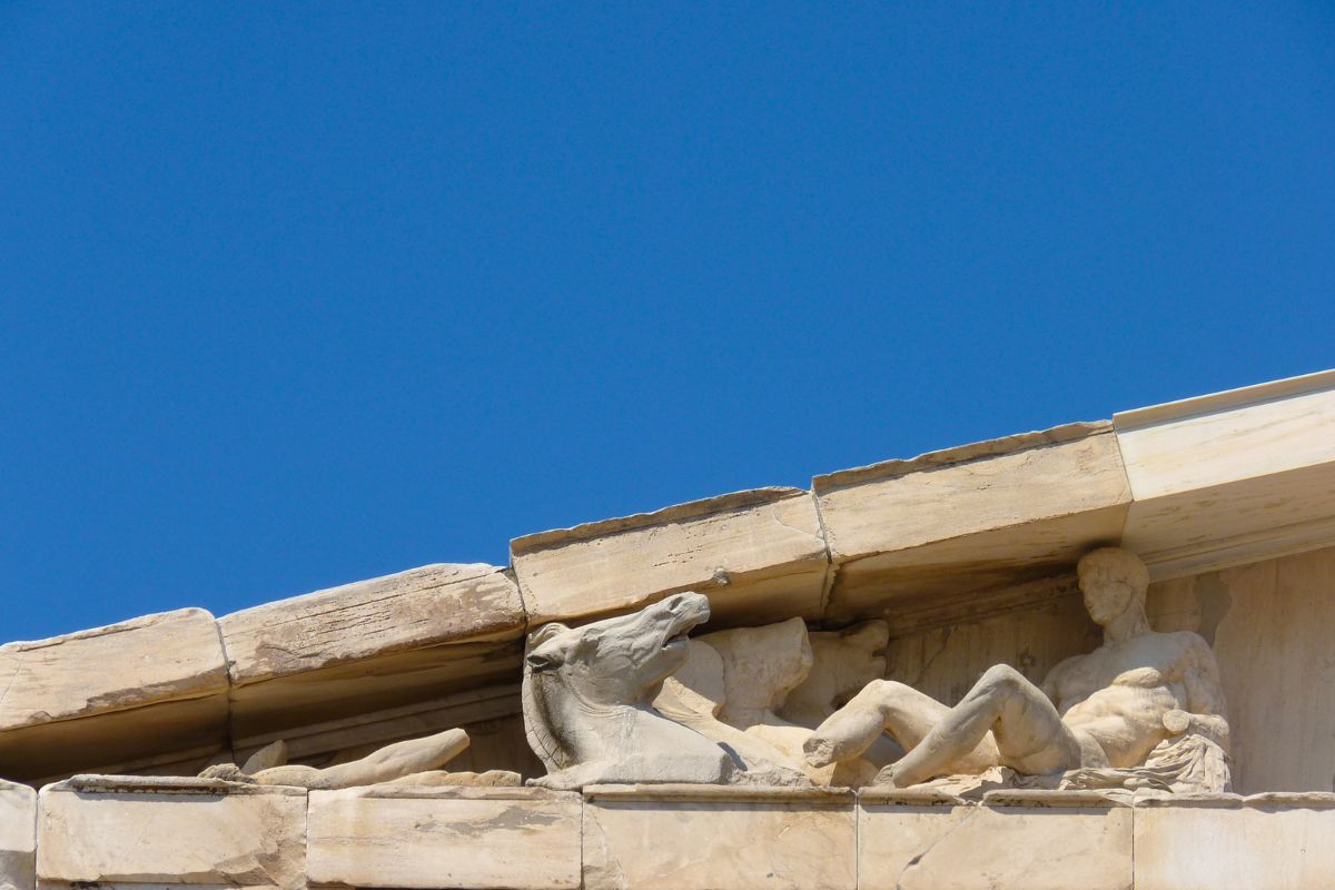 Detailed view of sculptures on the Parthenon in Athens, set against a clear blue sky.