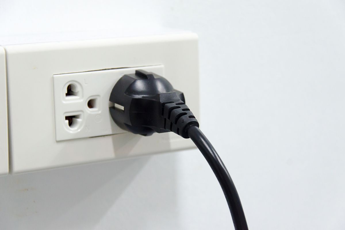 A black plug inserted into a white electrical socket on a wall.