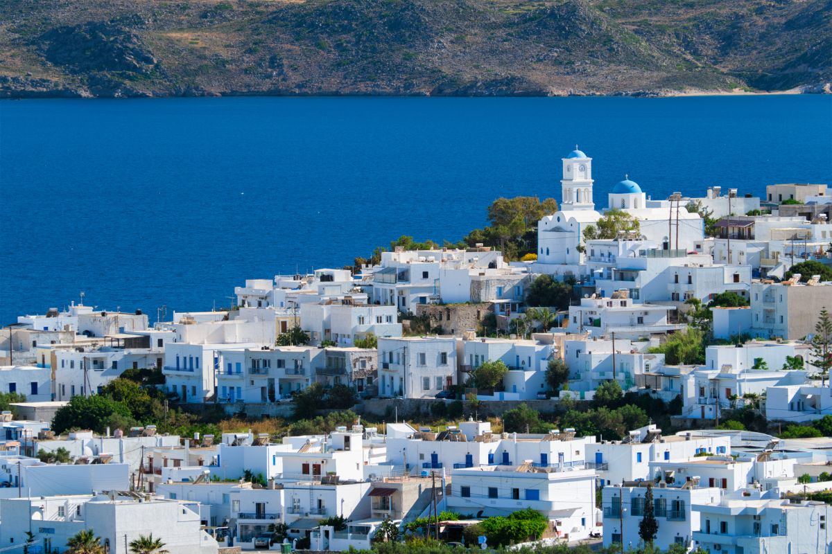 A picturesque view of Milos town with traditional white-washed buildings and blue-domed churches overlooking the vibrant blue waters of the Aegean Sea.