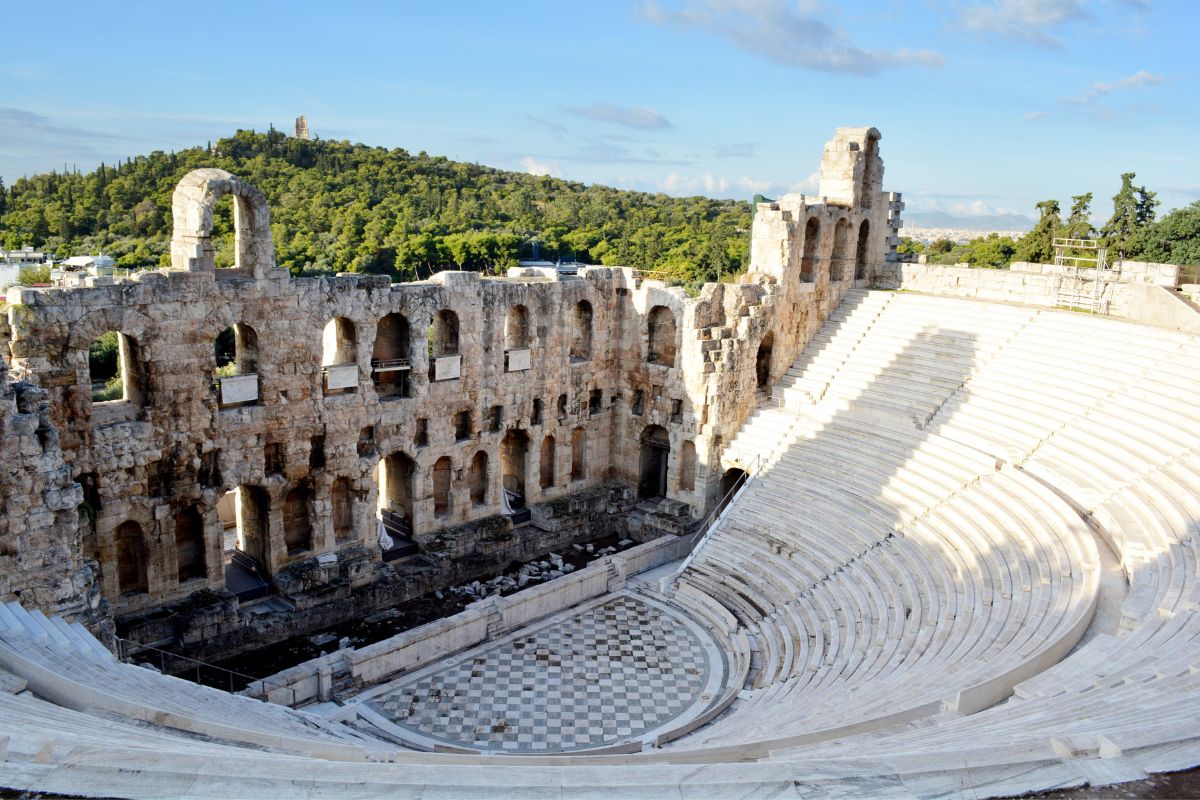 The Odeon of Herodes Atticus in Athens, showcasing its ancient stone structure and semi-circular seating area against a backdrop of green hills.