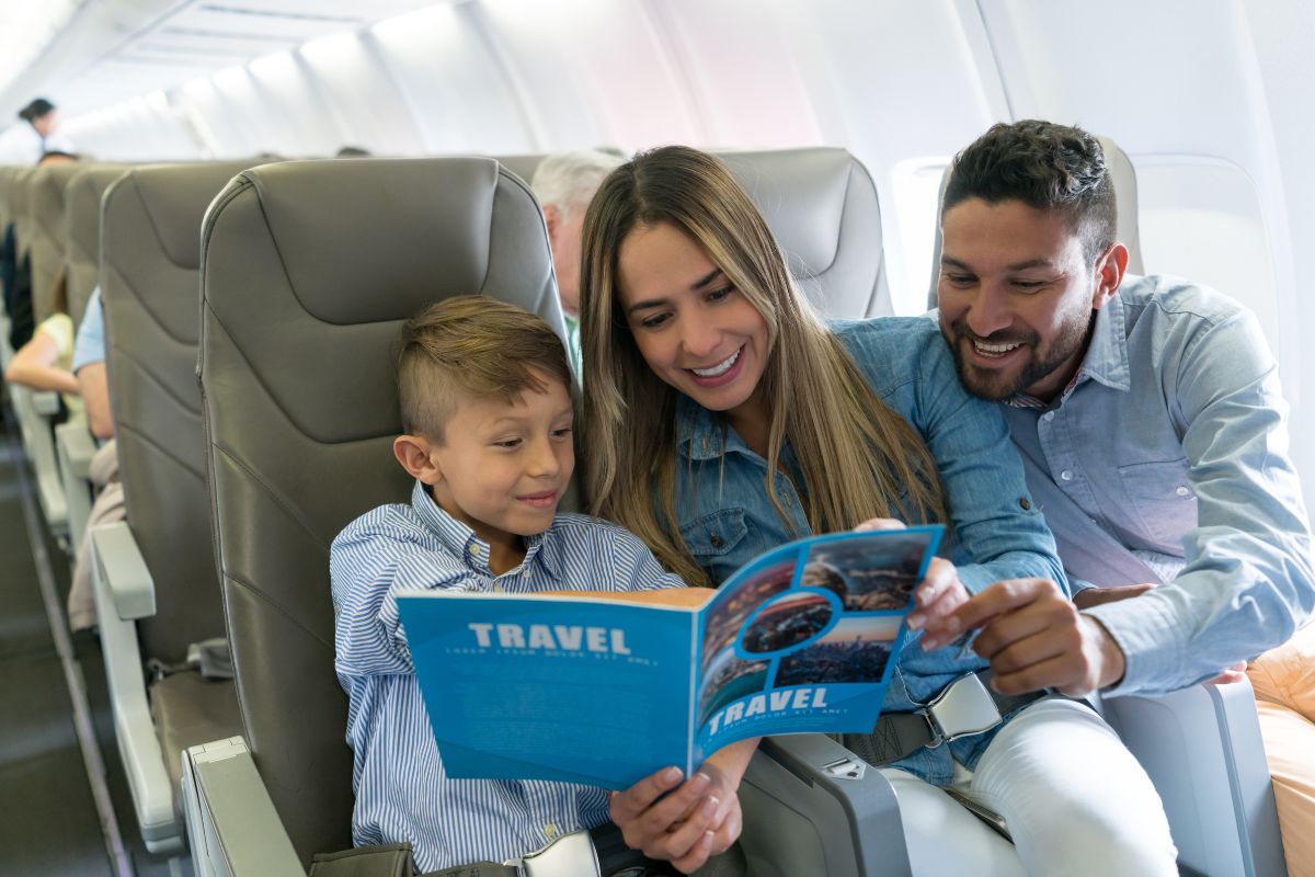 A smiling family sitting on an airplane, looking at a travel brochure together, creating a cheerful and engaging atmosphere.