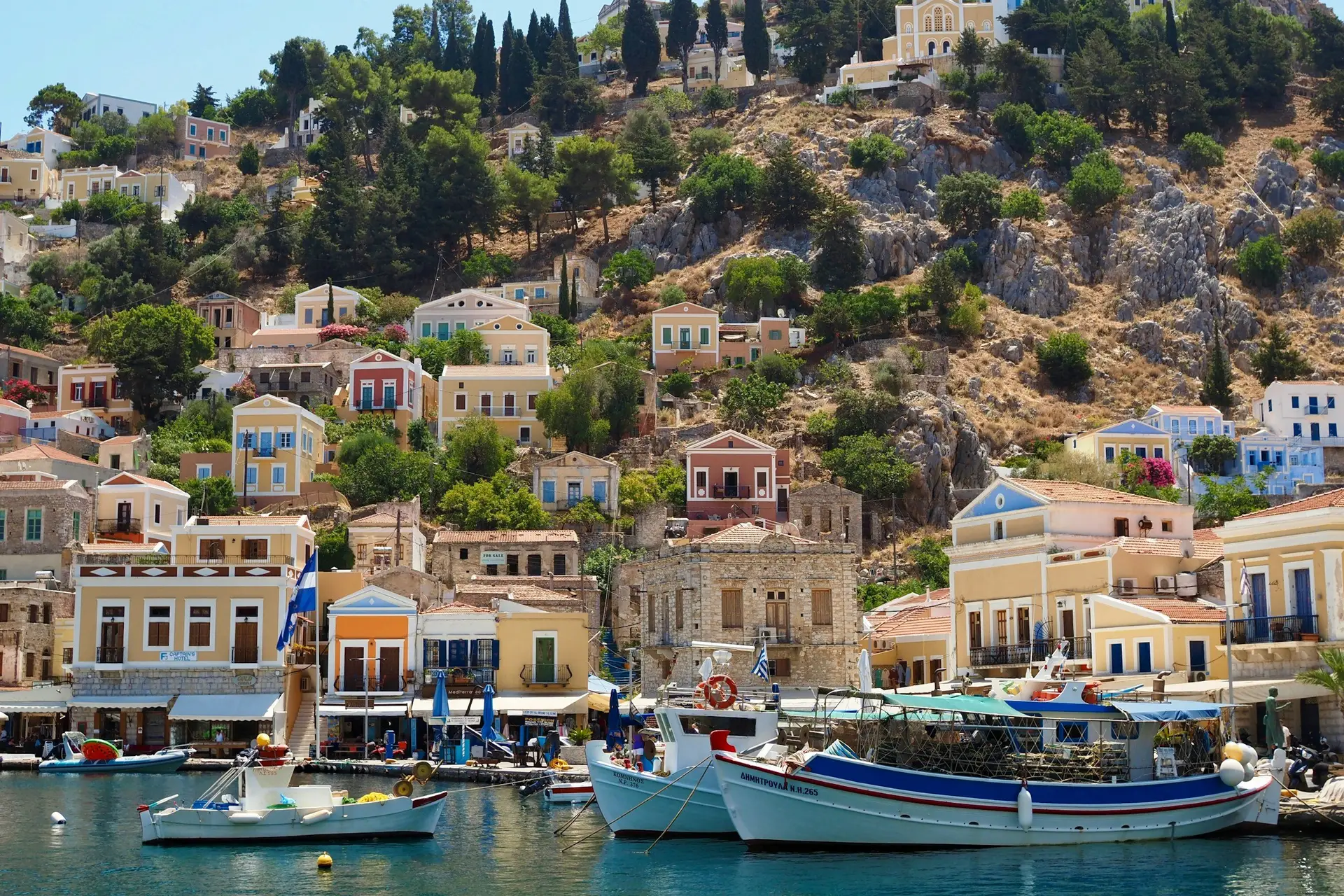 A blue and white boat anchored in a turquoise bay surrounded by pine trees
